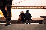 A guy and a girl sitting closely on the edge of a road in front of river.