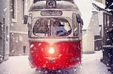 Red tram on a street in a light snow storm.