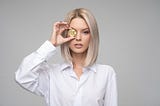 Photo of a woman holding a gold coin to her eye