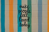 Sign with colored striped that says “Make people feel loved today.”