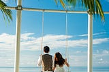 couple on large white swing on the beach, overlooking the sea on a gloriously sunny day