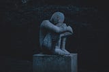 a stone statue of a human sitting down holding his knees, representing the emotion of grief
