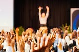 Male speaker andaudience with hands in the air