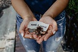 Woman’s hands cupped together holding coins and a note that says Make a Change