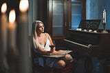 Woman wearing lingerie and holding wineglass sits near piano by candlelight