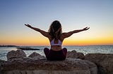 Woman doing yoga in front of the sea and sunset