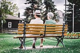 older man and woman sitting on a park bench with their back to the camera