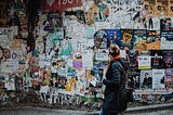 A woman looking at a wall filled with various posters, promo material, ads, etc.