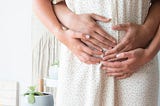 pregnant women in cream colored dress with partner during the first trimester