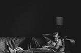 black and white photo of a person laying on a couch covering their face with their hand. They look exhausted.