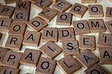 An array of Scrabble pieces (single letters with subscript point values) sit scattered across a wooden table, mid-game.