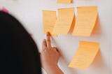 Person reading post-it notes stuck to a white wall.