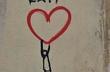 A stick figure dangling from a painted heart on a wall. The word EXIT written above.