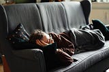 A woman laying on a gray couch wrapped in a gray blanket.