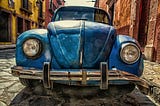 Photo of an old blue, beat-up car from the 1950s parked in an ally.