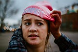 Young girl having a pink beanie placed on her head reading “FEMINIST” across the front.