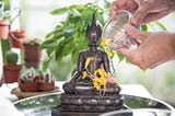 Person pouring floral water over Buddha statue