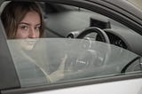 Young woman in the driving seat of a car. Hands on wheel, smiling.