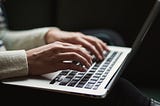 A close-up image shows a person poised with two hands hovering over a laptop keyboard, in the middle of typing.