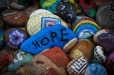 A bushel of pained rocks. One blue one has the word “HOPE.”