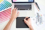 A designer working on a project with a laptop, stylus and colour swatches.