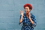 woman with curly short red hair and a big smile againse a blue wall