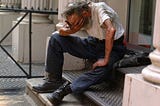 older man on the steps, holding his head in his hands, possibly crying