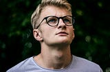 A blonde teenager boy with glasses looks upwards, in deep contemplation