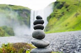 six small rocks balanced on top of each other in front of a waterfall