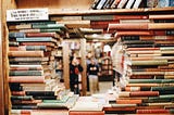 A shelf of books stacked with a hole in the middle to see through to people reading in the background