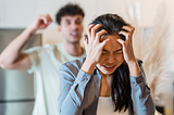 Woman holding her head in anguish as a man behind her yells