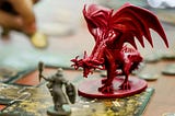Small red dragon figure and a smaller toy knight figure on a table indicating a game of Dungeons and Dragons.