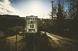 An image illustrating a speed limit sign on the side of a road, symbolizing the concept of setting limits for achieving success. The sign with the number “10” is placed on a pole, surrounded by a fence, under a bright sun. The empty road signifies the journey towards success, while the natural lighting adds a sense of optimism and possibility.