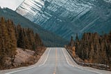 An open road leading to snow-capped mountains in the background.