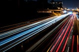 Long exposure picture of a highway, where the lights from the vehicles are really long continuous lines covering the road (and vehicles are actually not visible), giving a sense of really high speeds.