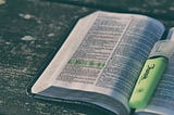 An open book filled with text, with a yellow highlighted passage on the left page. In the center of the book lies a yellow highlighter pen.