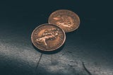 Two British pence on a dark background.