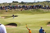 Golfer putting on edge of green with crowd behind