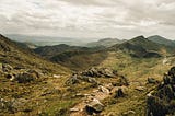 A landscape photograph of rural Wales, grey cloud in the sky and rock-covered hills and valleys.