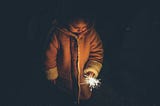 Child holding a sparkler in the darkness, her face lit by its glow