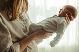 An partial view of a woman holding a newborn baby in her hands.