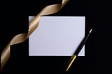 Blank Invitation, with a gold ribbon and a black, gold pen, on a black background.