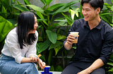 A guy together with a lady who is a yapper sitting on a bench enjoying their time together with coffee
