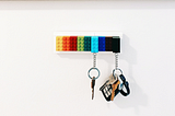 A couple of keys are suspended  from a row of colorful legos that form a key hook.