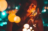 A woman with a hat holding a string of light. She looks calm and content.