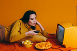 A woman in a yellow long-sleeved shirt lying on her side while watching something on a Yellow TV
