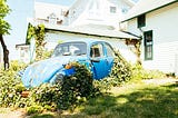 A blue Volkwagen sitting with plants growing out of it