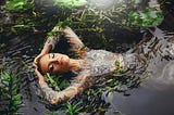 A woman floating in a lake surrounded by vegetation.