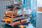 A pile of books with string lights around it and a candle on top.