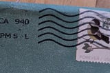 Books, Writing, and other Adventures: An image of the upper corner of a turquoise envelope, with a stamp obscured by black wavy postage marks.